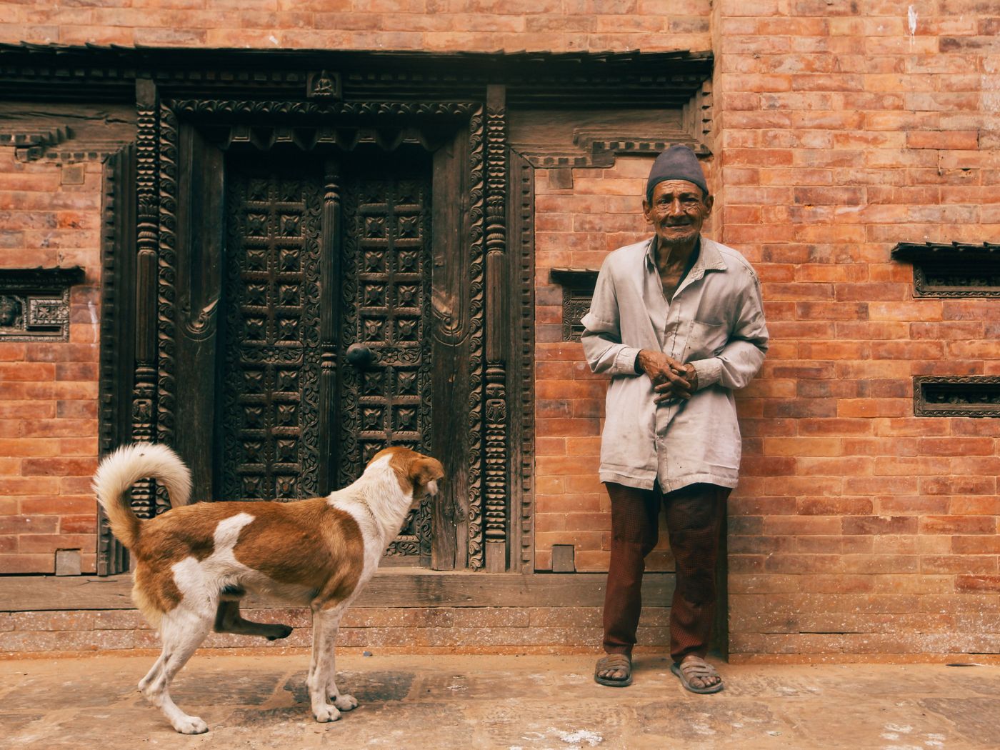 A person standing with a dog outside a wooden doorway.
