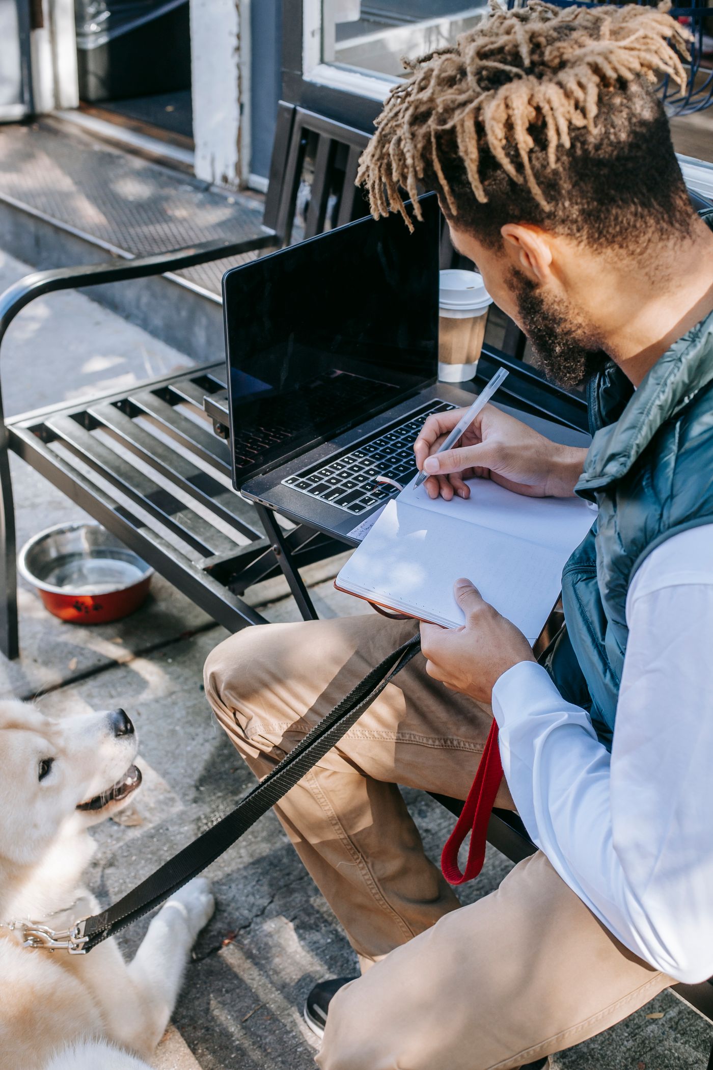 A person writing in a notebook with a dog beside them.